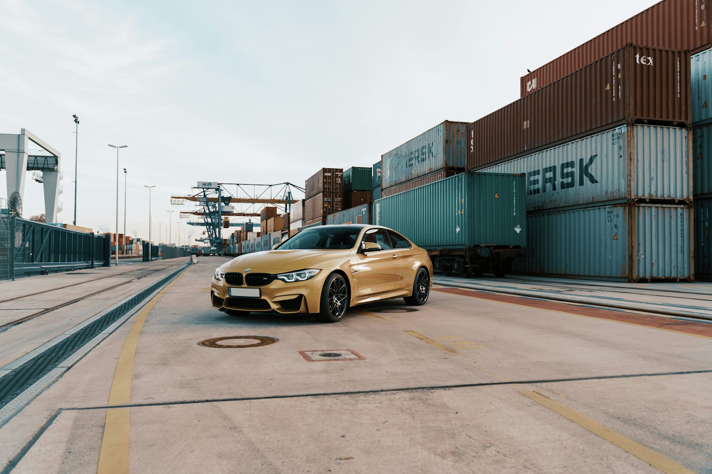 Golden sports car parked on concrete near shipping containers.