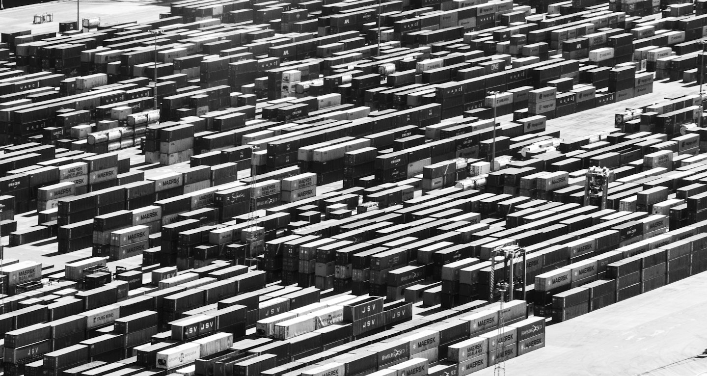 Rows of stacked shipping containers fill a busy industrial yard.