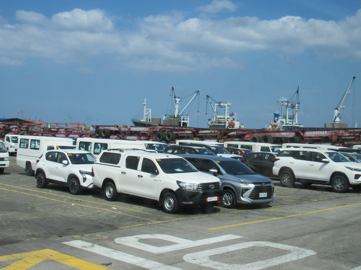 Rows of white vehicles parked at a busy shipping port.