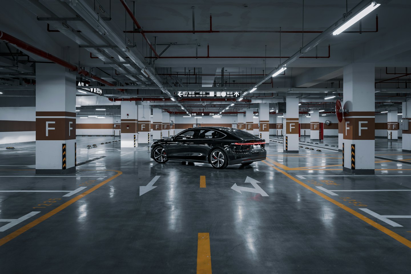A black sedan parked inside a brightly lit concrete garage.