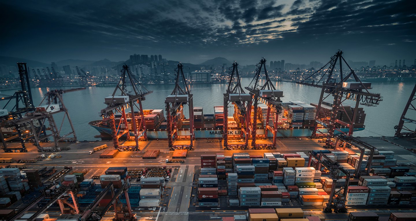 Gantry cranes load cargo ship at busy port at dusk.