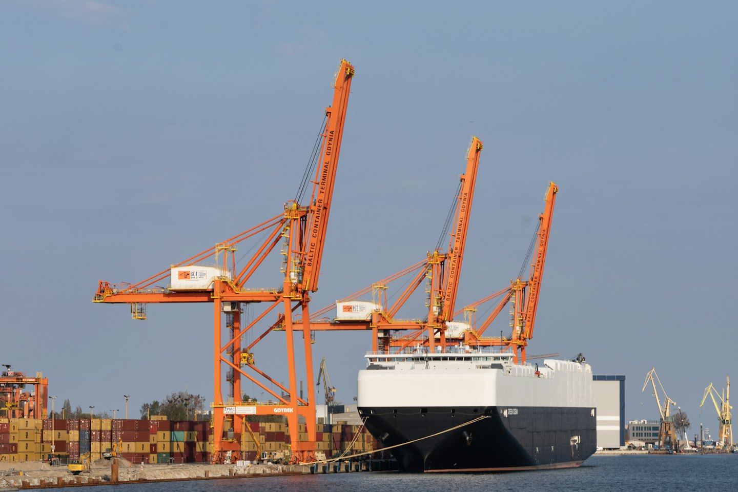 A large cargo ship docks at an industrial port with cranes.
